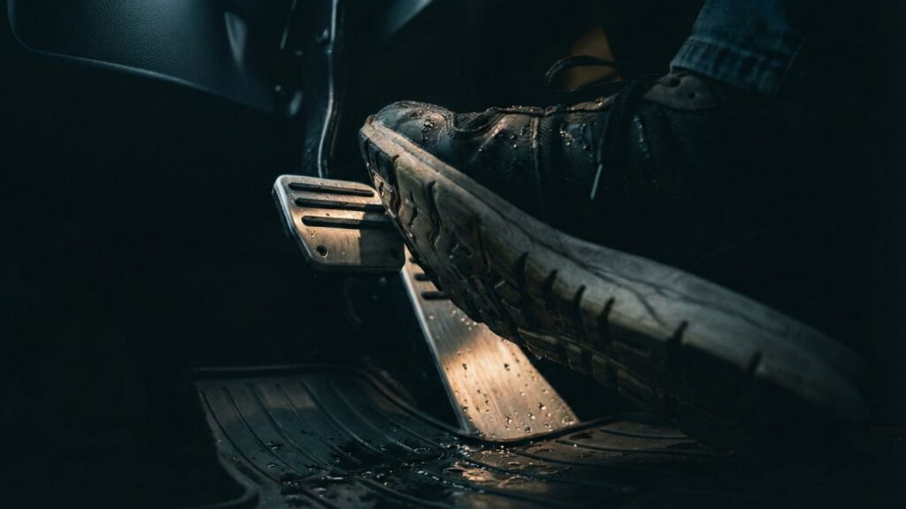 雨の日に濡れた靴底でアルミ製のペダルカバーを踏み込み、滑って操作ミスをしそうになる危険な運転席の足元のクローズアップ写真。